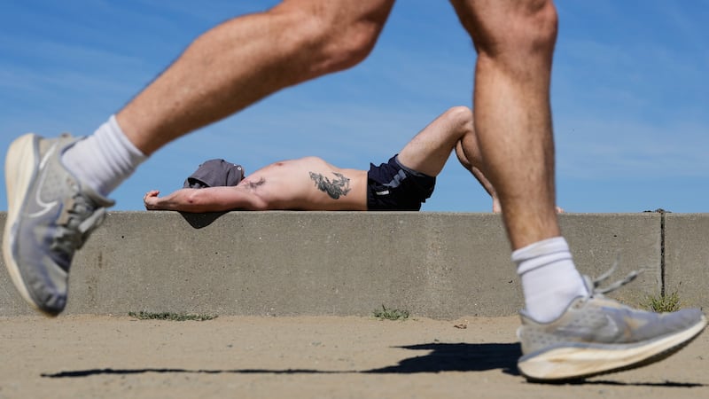 ARCHIVO - Un corredor pasa mientras un hombre toma el sol en un día caluroso en Crissy Field,...